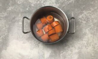 Морковь тщательно помойте, очистите от кожуры, разрежьте на несколько частей, переложите к кастрюлю и залейте водой.